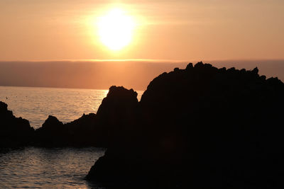 Silhouette rocks by sea against sky during sunset