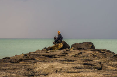 Woman sitting on rock by sea against clear sky