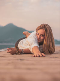 Portrait of young woman relaxing against sky during sunset