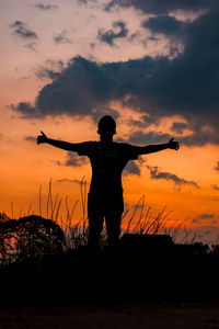 Silhouette woman standing against orange sky during sunset