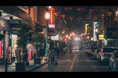 People on illuminated street amidst buildings in city at night