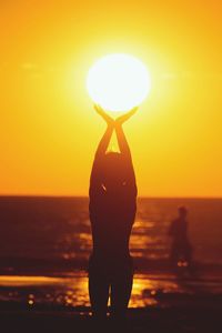 Optical illusion of silhouette girl holding sun at beach during sunset