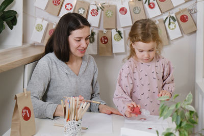 Mother with toddler child writing christmas letter and doing advent calendar tasks in kids room