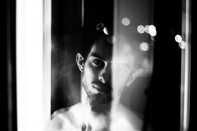 Portrait of shirtless young man looking through window at home