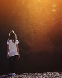 Full length rear view of teenage girl standing on riverbank during sunset