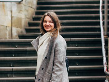 Portrait of smiling young woman standing against steps