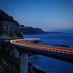 Light trails on sea cliff bridge against sky at dusk