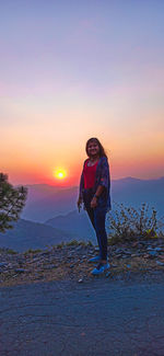 Woman standing on mountain against sky during sunset