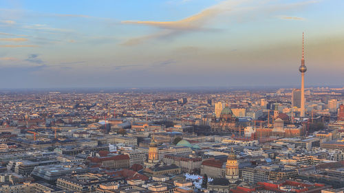 Fernsehturm amidst cityscape against sky during sunset