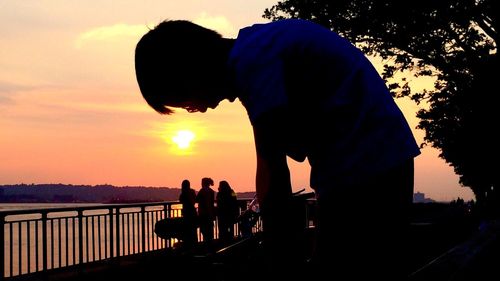 Silhouette people standing by sea against sky during sunset