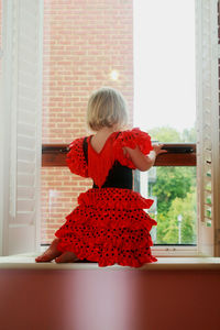 Girl looking away while standing against window at home