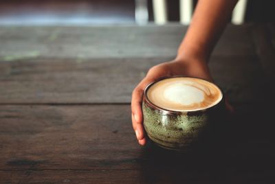 Cropped hand of person holding coffee cup on table