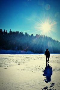 Silhouette man walking on snowy landscape against sky during winter