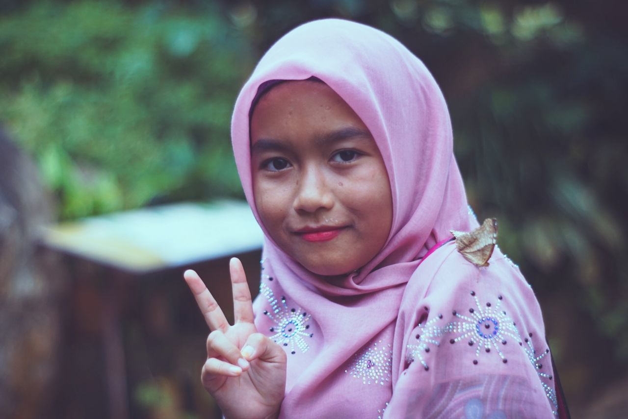 one person, front view, real people, headshot, portrait, headscarf, pink color, focus on foreground, childhood, lifestyles, hijab, leisure activity, child, looking at camera, day, women, females, traditional clothing, close-up, innocence, outdoors, hood - clothing, purple