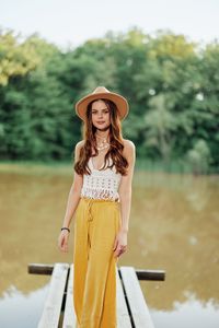 Portrait of young woman wearing hat standing against trees