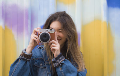 Portrait of smiling woman holding camera against curtain