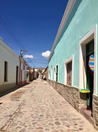 Footpath amidst buildings against blue sky