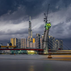 Illuminated buildings by river against sky in city at dusk