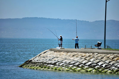 Men fishing in sea against clear sky