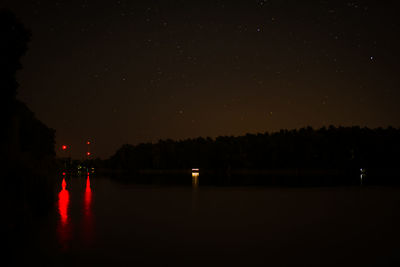 Silhouette trees by lake against sky at night