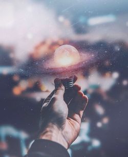 Close-up of hand holding hands against sky at night