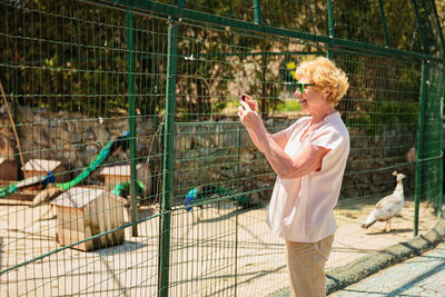 Elderly woman with mobile smartphone taking photo in zoo