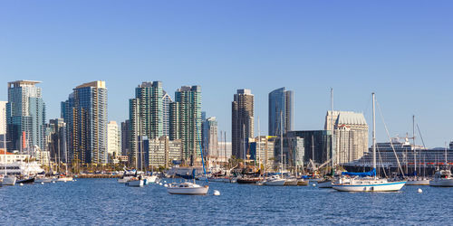 Sailboats in sea by modern buildings against clear sky