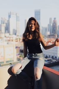 Young woman wearing torn jeans standing against building in terrace