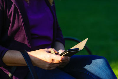 Caucasian blond woman searching on the phone outside, outdoor. adult woman in purple blouse in park 