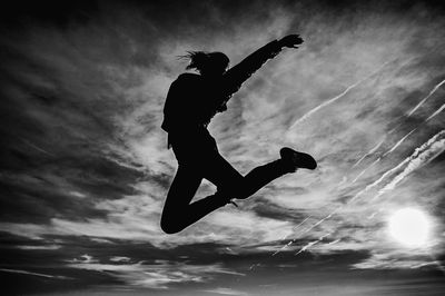 Low angle view of silhouette woman jumping against sky