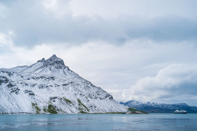 Scenic view of sea by mountain against sky