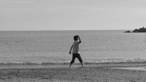 Rear view of playful boy on sea shore against sky