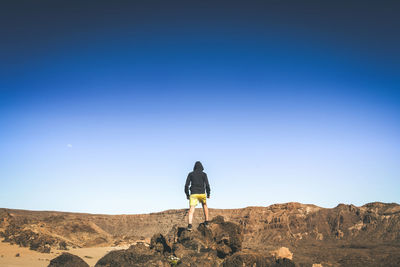 Rear view of boy standing on rocks against clear sky