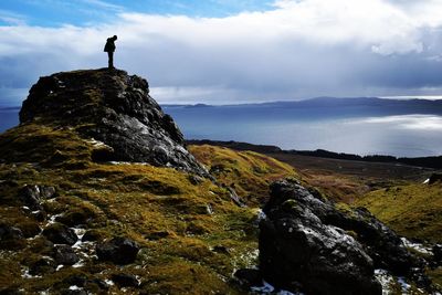 Rear view of man standing on rock against sky