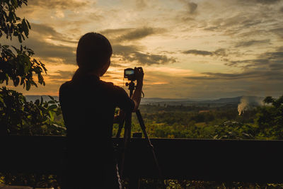 Silhouette woman photographing landscape against sky during sunset