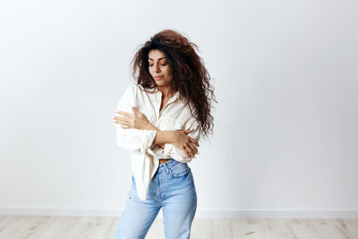 Woman with arms crossed posing in front of white wall