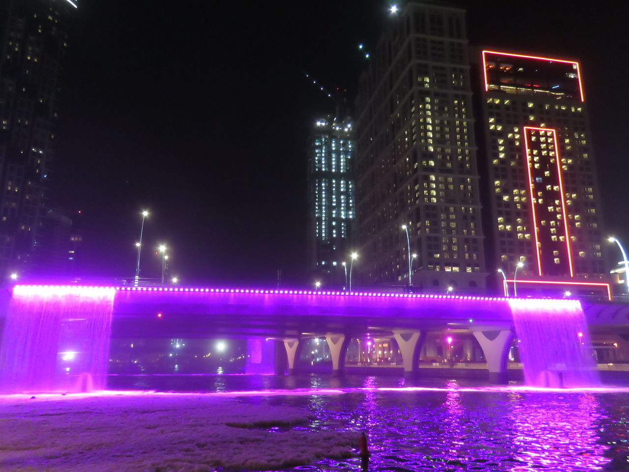 ILLUMINATED CITY BY RIVER AGAINST SKY AT NIGHT