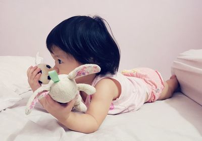 Cute baby girl looking away while lying on bed against wall at home