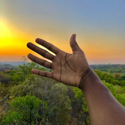 Cropped hand of man against sky during sunset