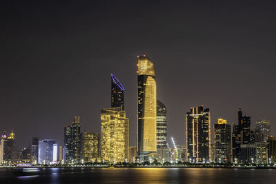 Illuminated modern buildings in city against sky at night