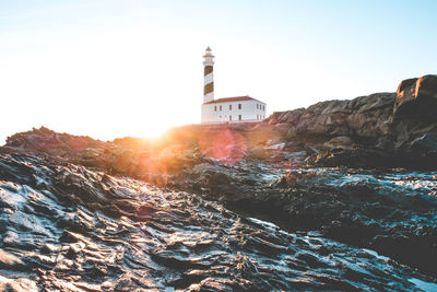 Lighthouse by sea and buildings against clear sky