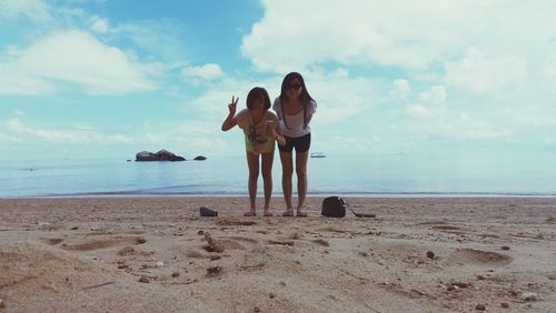 Full length of friends bending on shore at beach against cloudy sky