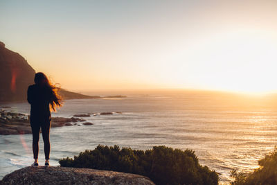 Rear view of woman standing on beach against sky during sunset