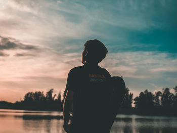 Rear view of silhouette man standing by lake against sky