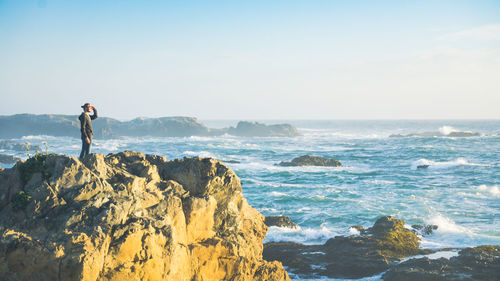 Side view of man standing on cliff by sea against sky