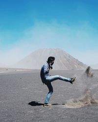 Side view of young man playing on sand against blue sky