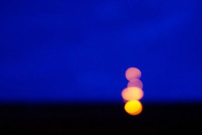 Low angle view of illuminated moon against blue sky at night