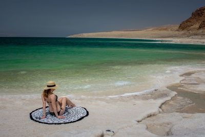 Woman sitting at beach against sky