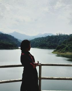 Man standing by railing on lake against sky