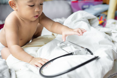 Cute baby boy playing with stethoscope while sitting on bed at home